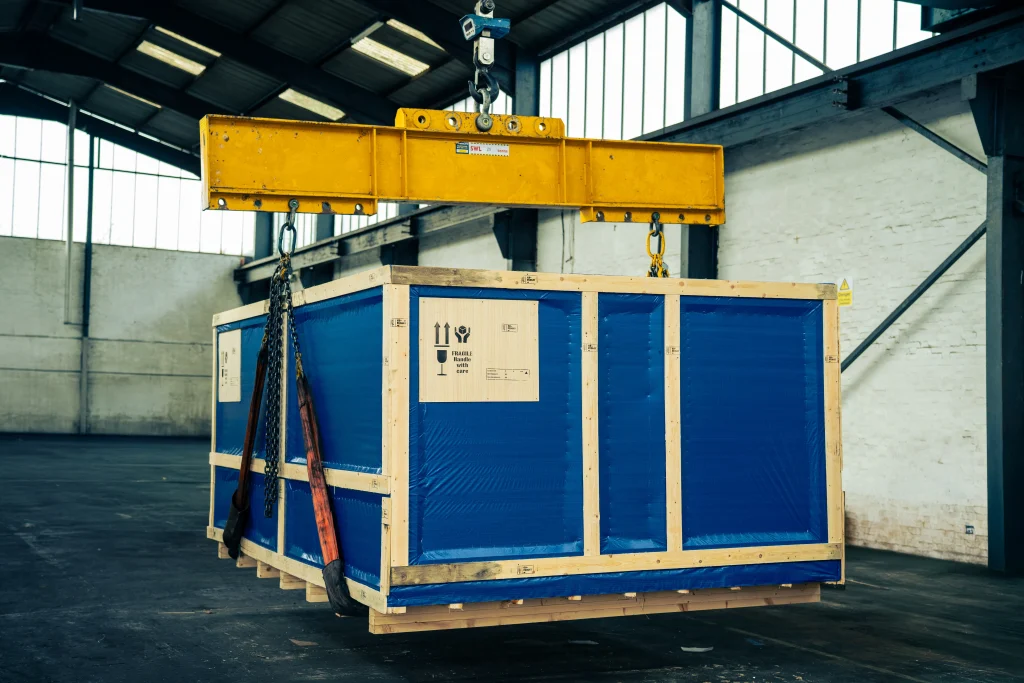 Factory relocation crate being lifted by overhead crane inside warehouse